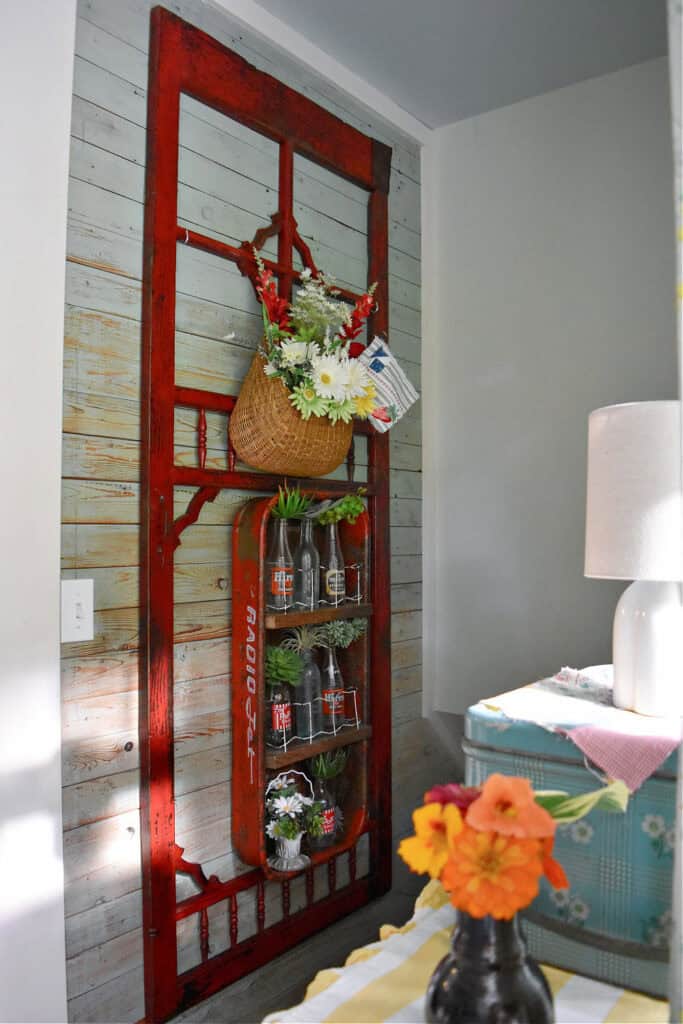Antique red screen door hanging in entry with upcycled wagon shelf.