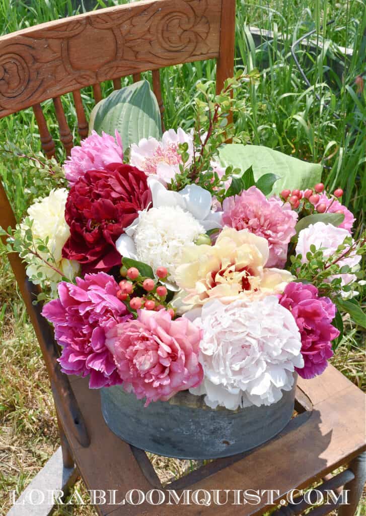 Peony floral arrangement in metal bucket on chair.