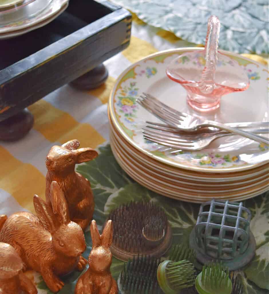 Vintage stack of plates, floral frogs and gold bunnies for Easter table setting.