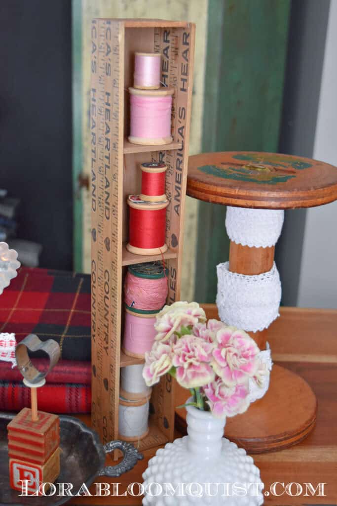 Pink and red wooden thread spools on yardstick shelf in craft room.