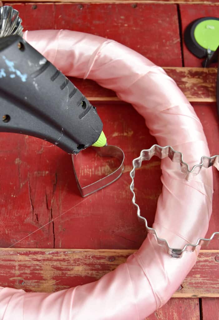 Gluing old cookie cutters to pink satin Valentines wreath.