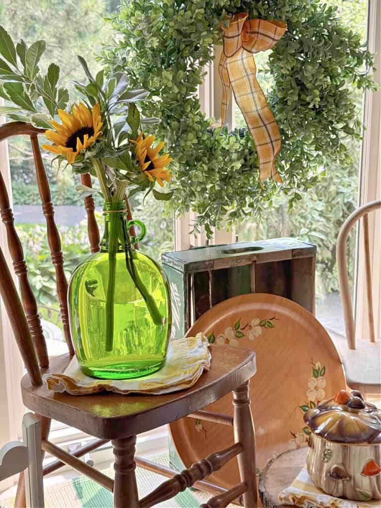 Sunflowers in green glass bottle sitting on antique childs chair.