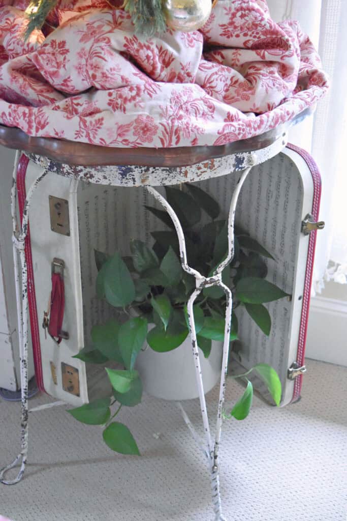 Shabby white metal table with plant and vintage suitcase.