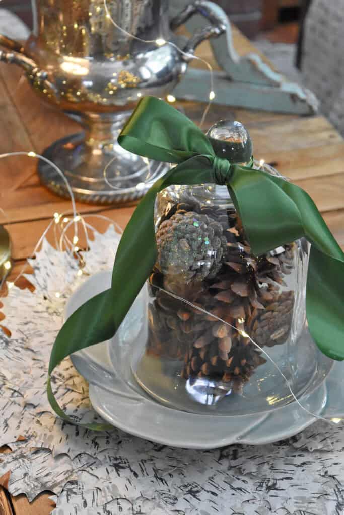 Glass cloche with pinecones and green ribbon.